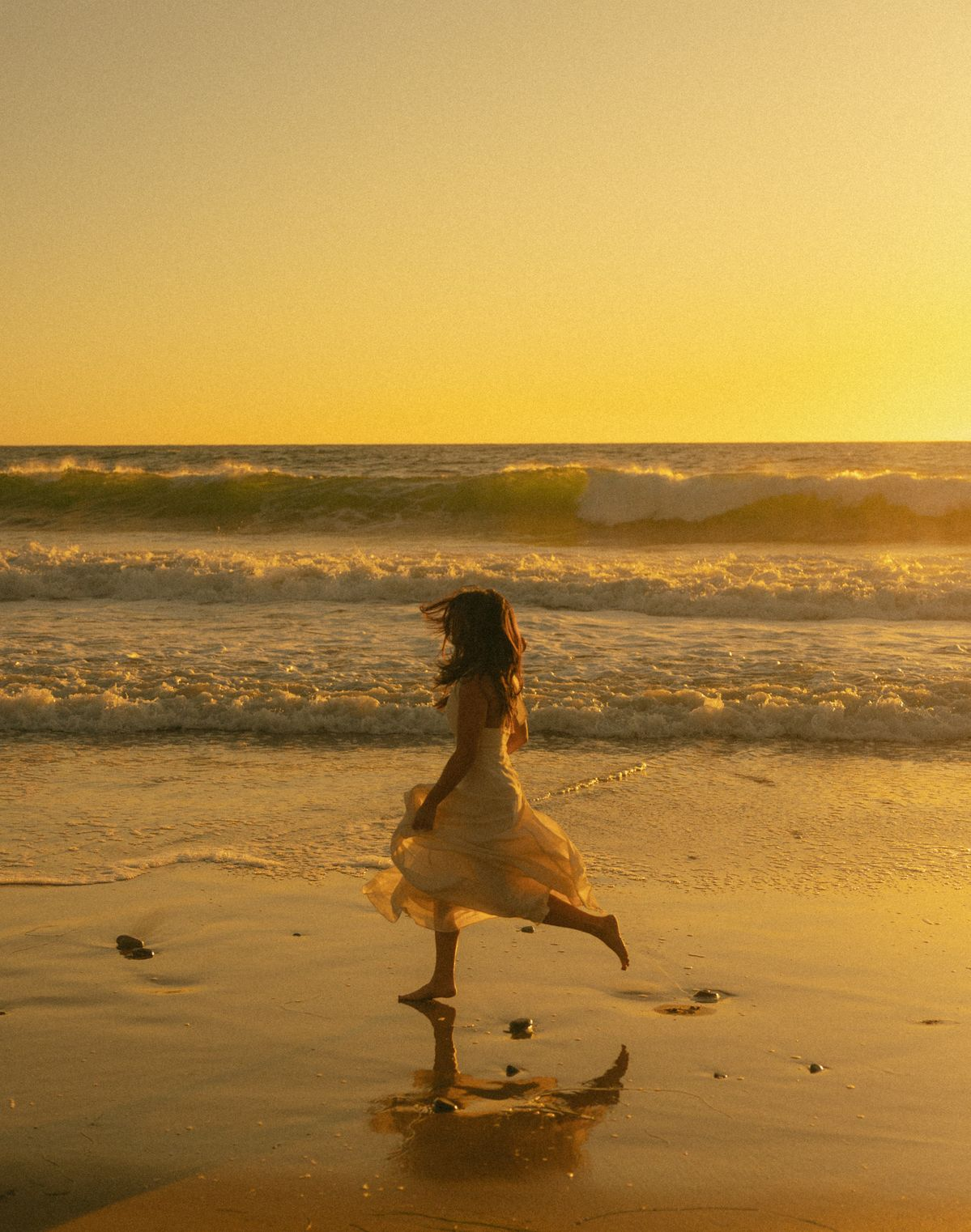 A young woman standing on the beach at sunset, seen from behind